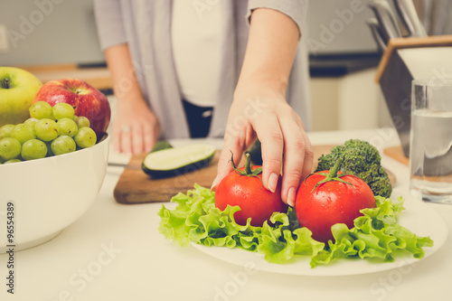 toned photo of woman picking fresh tomato from table on kitchen