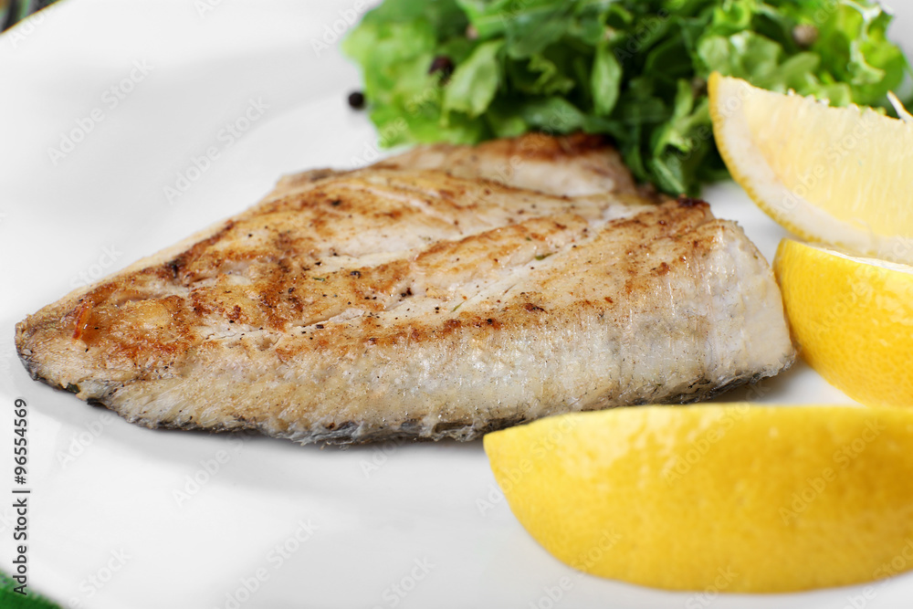 Dish of fish fillet with greens and lemon on plate close up Dish of fish fillet with greens and lemon on plate close up