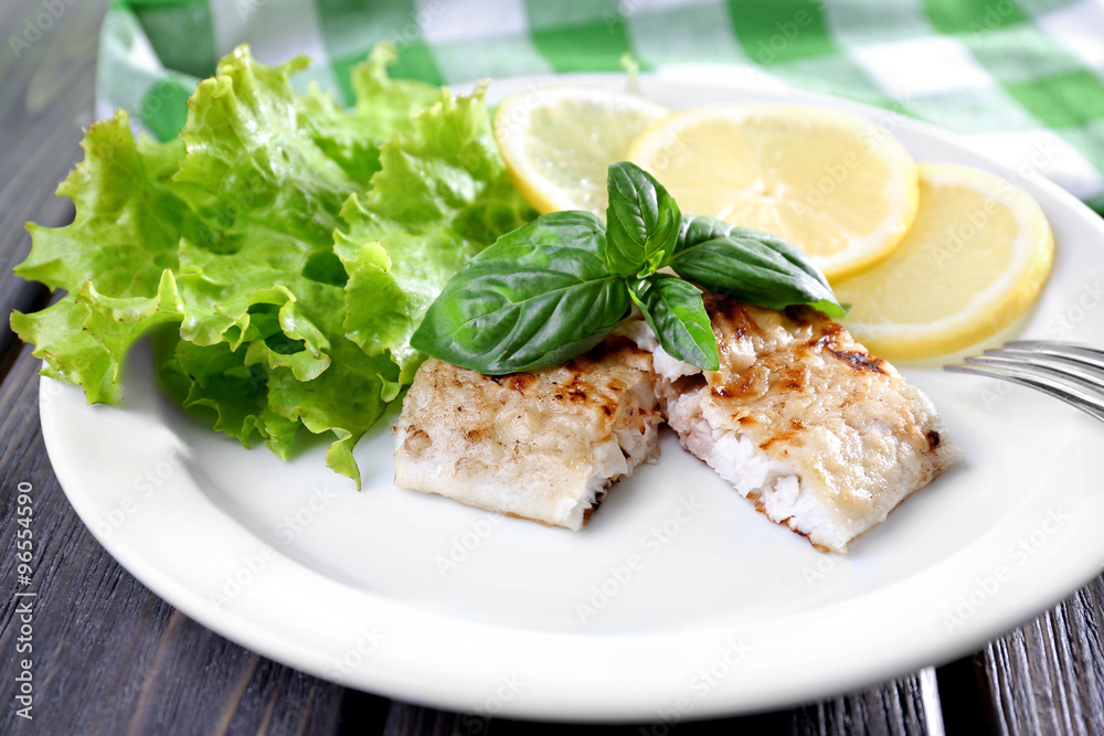 Dish of fish fillet with greens and lemon on plate close up Dish of fish fillet with greens and lemon on plate close up