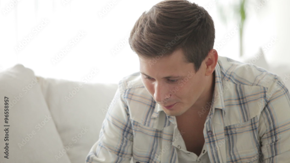 Attractive guy sitting on sofa with laptop eating apple and looking at camera with smile Attractive guy sitting on sofa with laptop eating apple and looking at camera with smile
