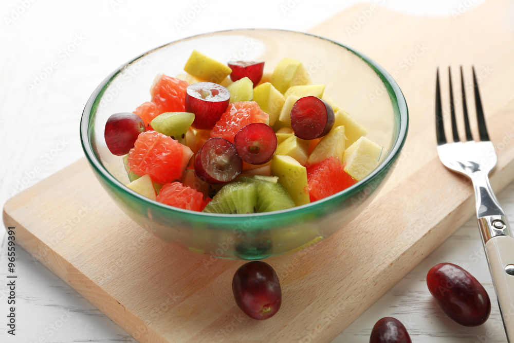 Fruit salad in glass bowl, on light wooden background Fruit salad in glass bowl, on light wooden background