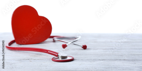 red stethoscope with heart on bright wooden table isolated on white