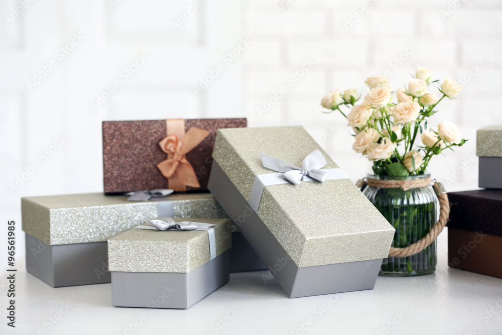 Fototapeta premium Beautiful gift boxes with bouquet of flowers on the table in front of brick wall, close up