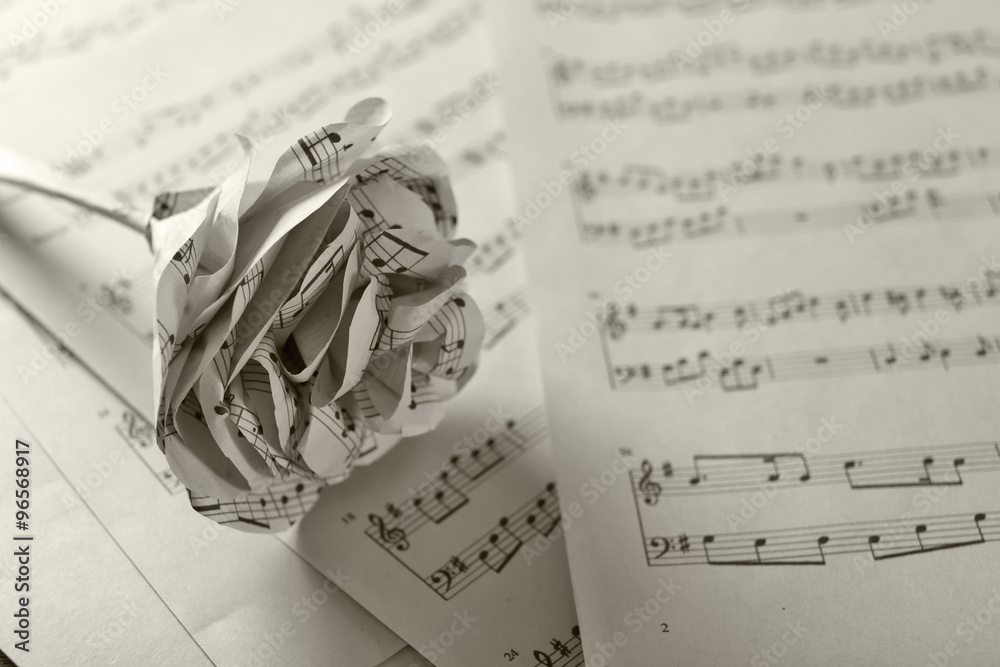 Naklejka premium Single white paper-made rose on musical notes pages background
