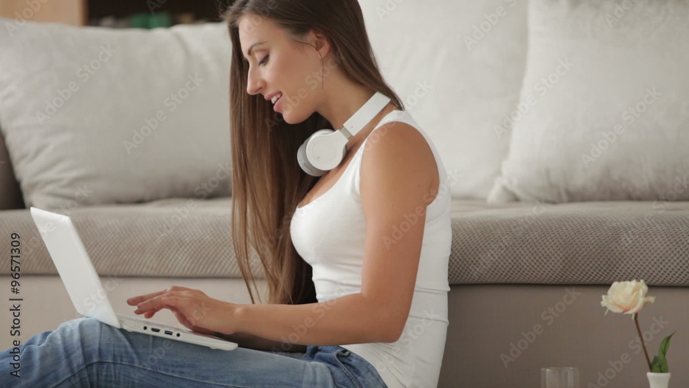 Young woman in headset sitting on floor and using laptop Young woman in headset sitting on floor and using laptop
