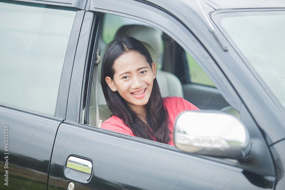 Young Asian woman driving a car, smiling to the camera