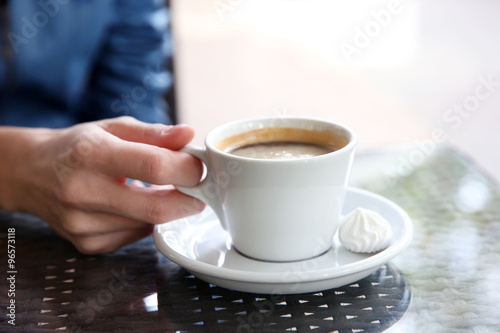 Cup of coffee with hands and zephyr on table in cafe background