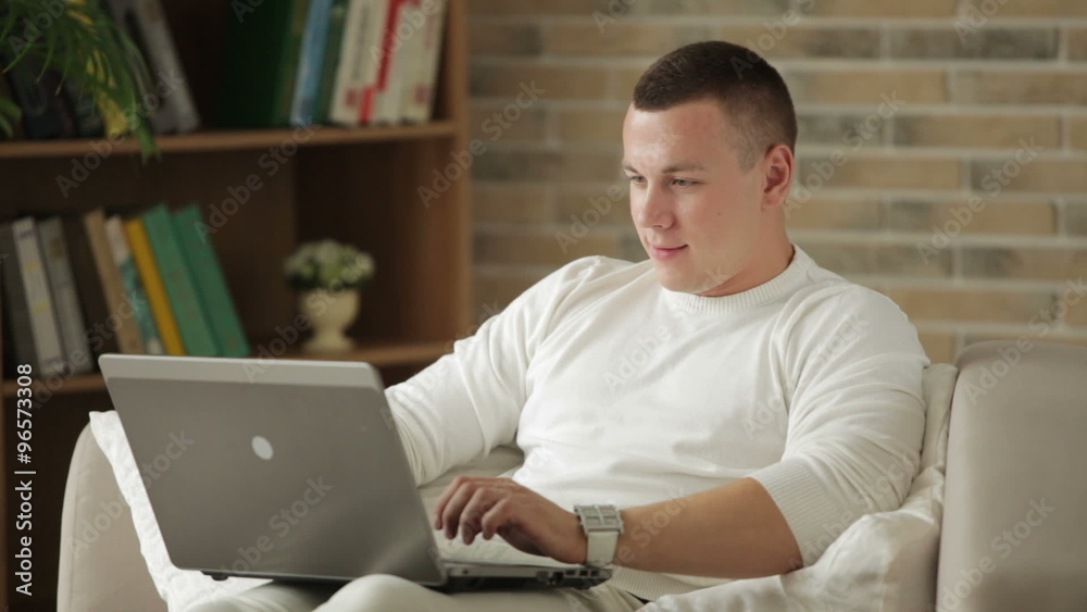 Handsome guy sitting on couch with laptop holding credit card and smiling Handsome guy sitting on couch with laptop holding credit card and smiling