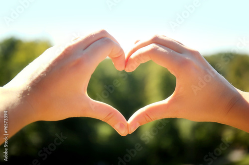 Woman holds hands up in the shape of a heart on nature background