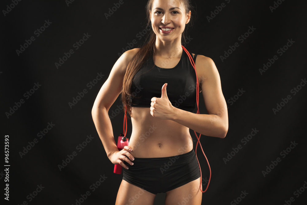 Muscular young woman athlete with a skipping rope on black Muscular young woman athlete with a skipping rope on black