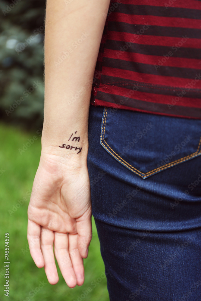 Hand of young woman with tattooed phrase on it, on green grass background, close-up