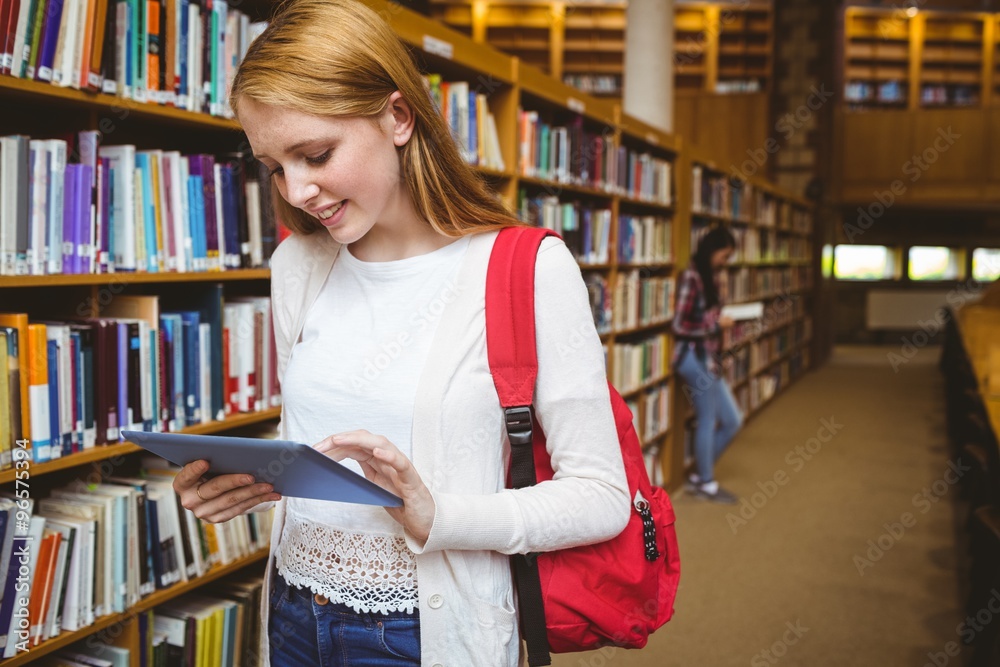 Smiling student with backpack using tablet in library Smiling student with backpack using tablet in library