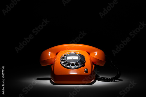 orange retro phone in spotlight on black background