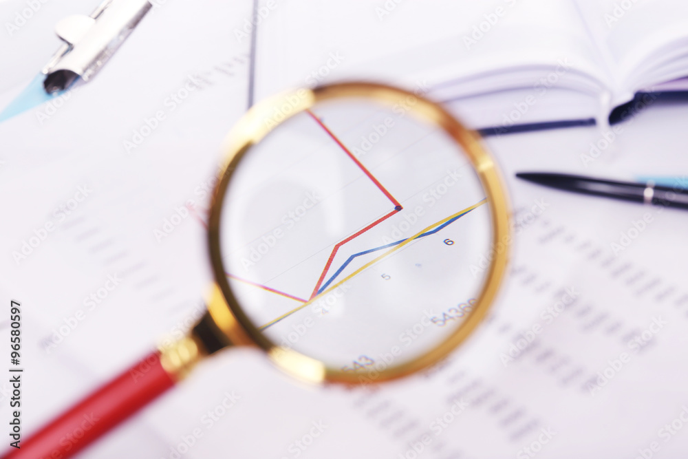 A magnifying glass on financial documents background, close-up
