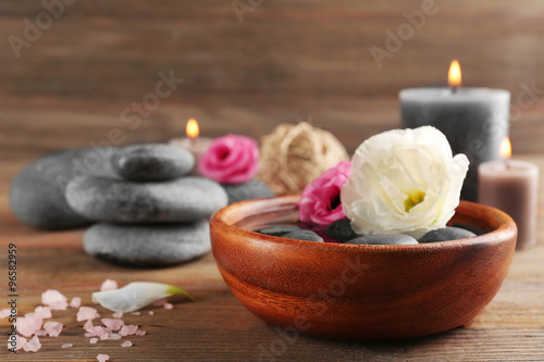 Beautiful composition of aroma candle with pebbles and flower in a bowl on wooden background