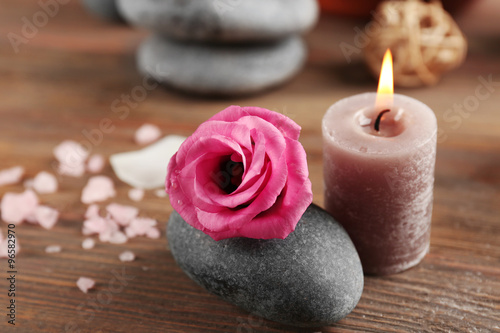 Beautiful composition of aroma candle with pebbles and flower on wooden background