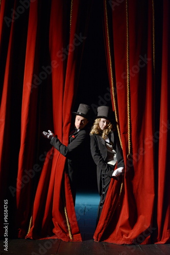actor and actress in tuxedos open the stage curtain
