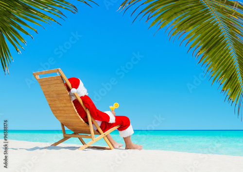 Christmas Santa Claus with cocktail on deckchair at tropical beach