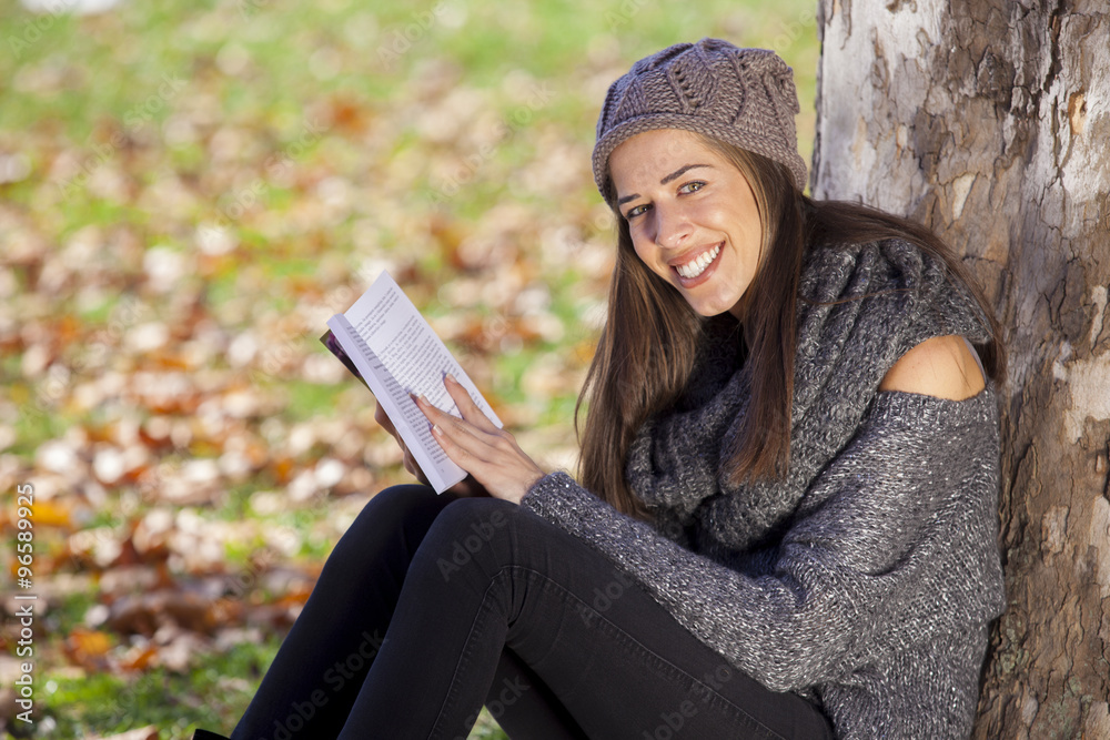 Obraz premium Young girl reading a book lying in the grass on the leaves in the autumn park