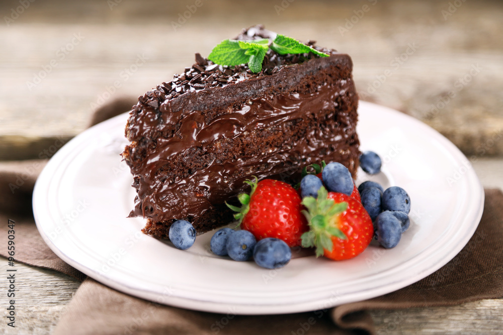 Chocolate cake with chocolate cream and fresh berries on plate, on wooden background Chocolate cake with chocolate cream and fresh berries on plate, on wooden background