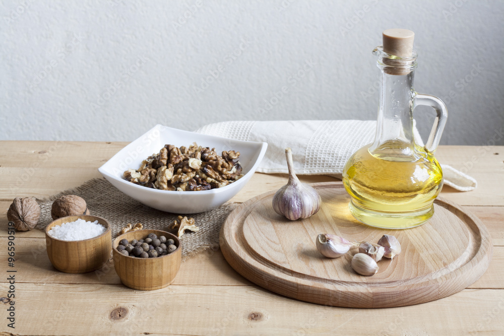 Walnuts in a white bowl, garlic, pepper salt and oil on a wooden background, wooden board and white napkin