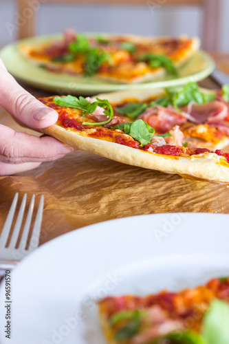 Female hand grabs for a slice of italian style pizza with arugula and prosciutto