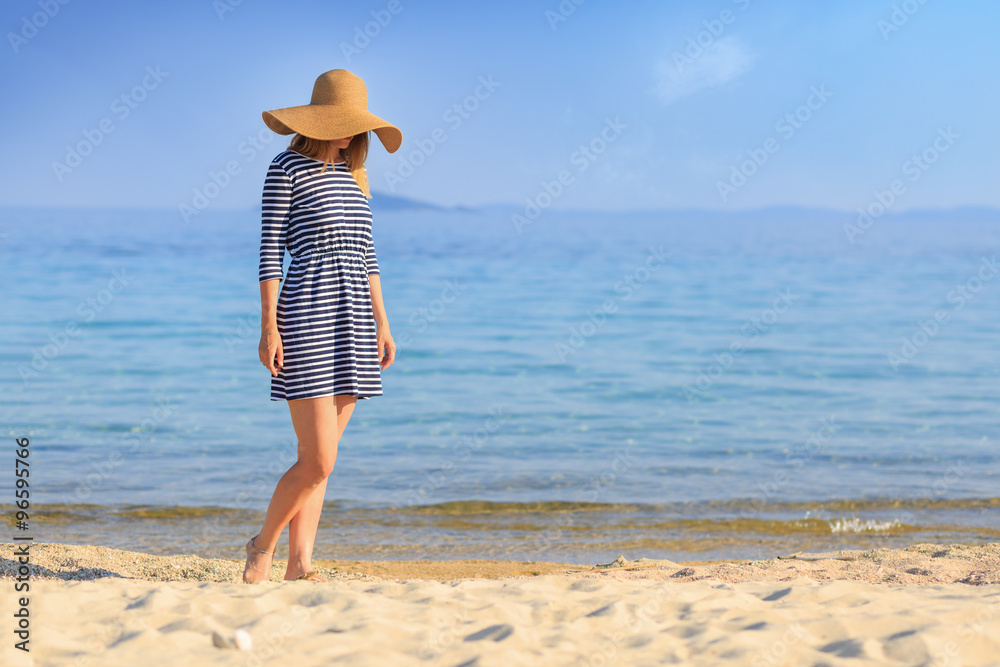 Portrait of a woman with a straw hat walking barefoot at the beach