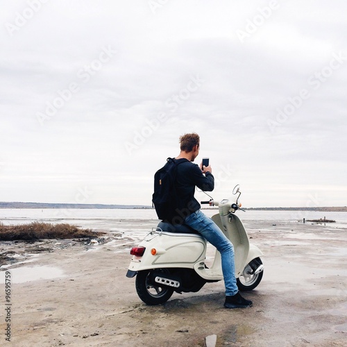 hipster man make phone photo on motocycle on the sea beach