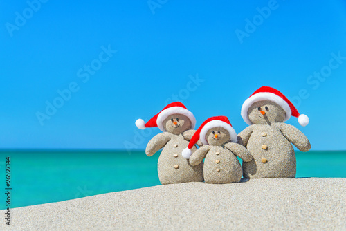 Family of Snowmen in santa hats at tropical beach. Christmas con