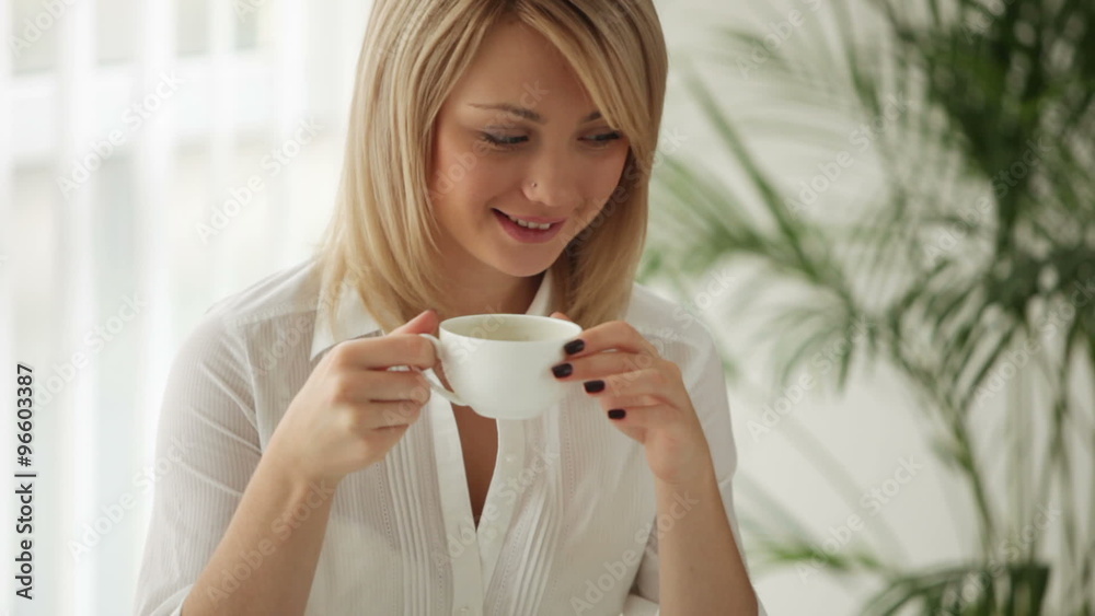 Pretty young woman sitting at table drinking coffee and smiling at camera Pretty young woman sitting at table drinking coffee and smiling at camera