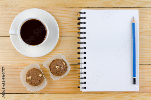 A blank white notebook and cup of coffee and pencil with cookie on the wooden table