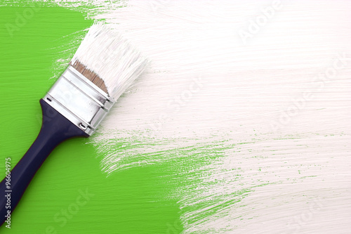 Paintbrush with white paint painting over green
