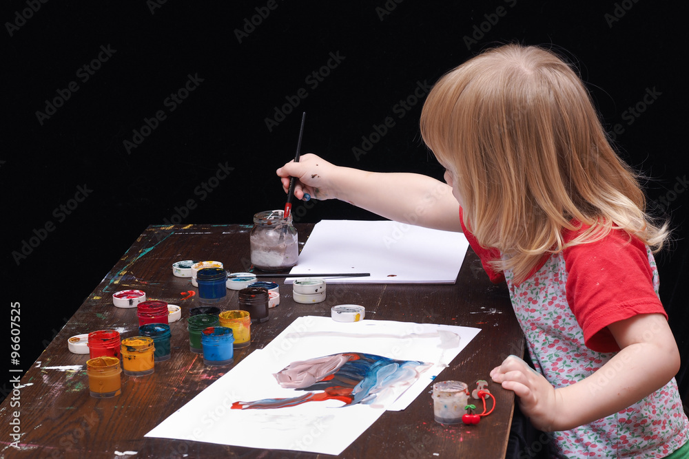 Маленький ребенок рисует красками, гуашью. Темный стол в краске, банки с  краской. Девочка рисует кистью на белой бумаге. Черный фон. У девочки  светлые волосы, она очень мала Stock Photo | Adobe Stock