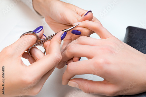 Beautician make the manicure with scissors
