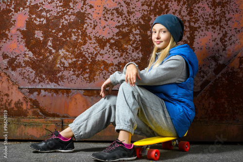 Smiling girl sitting on color plastic penny board or skateboards outdoor