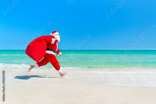 Santa Claus running along beach with sack full of gifts