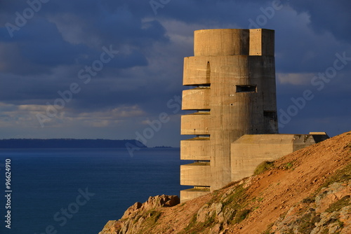 WW2 German bunker, Jersey, U.K.  Telephoto image of an uninhabited ruin of a radio tower from WW2, lit by an Autumnal sunset with moody skies and the Isle of Sark in the distance. photo