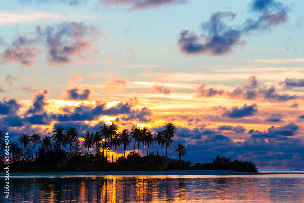 Beautiful sunset with dark silhouettes of palm trees and amazing cloudy sky in tropical island Beautiful sunset with dark silhouettes of palm trees and amazing cloudy sky in tropical island