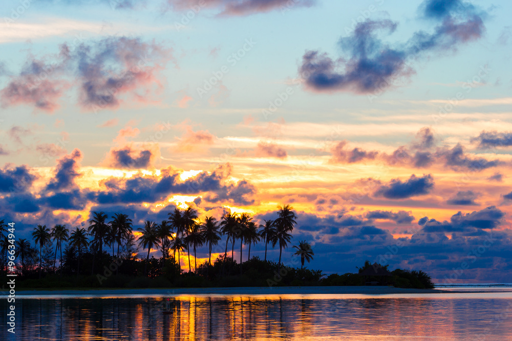 Beautiful sunset with dark silhouettes of palm trees and amazing cloudy sky in tropical island