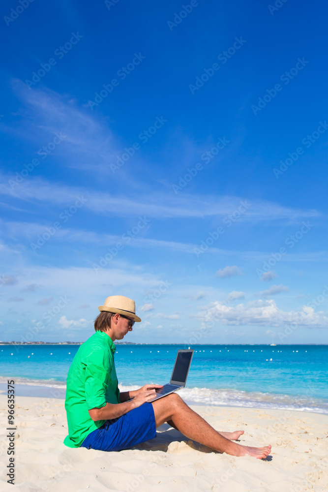 Young man with laptop on white tropical beach