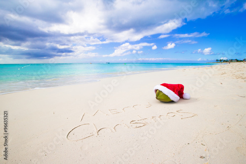 Merry Christmas written on beach white sand with red Santa hat