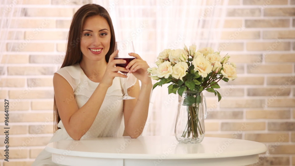 Beautiful young woman sitting at cafe holding glass of wine and smiling at camera. Panning camera Beautiful young woman sitting at cafe holding glass of wine and smiling at camera. Panning camera