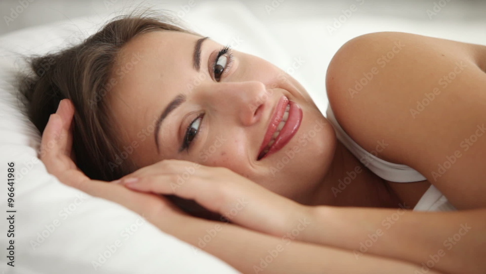 Charming girl relaxing in bed looking at camera and smiling. Panning camera Charming girl relaxing in bed looking at camera and smiling. Panning camera