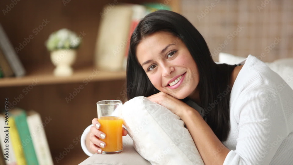 Cheerful girl relaxing on sofa holding glass of juice looking at camera and smiling. Panning camera Cheerful girl relaxing on sofa holding glass of juice looking at camera and smiling. Panning camera