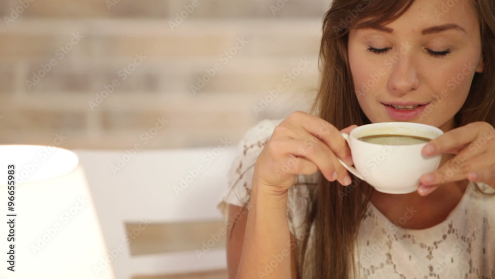Beautiful young woman sitting at cafe drinking tea looking at camera and smiling. Panning camera Beautiful young woman sitting at cafe drinking tea looking at camera and smiling. Panning camera