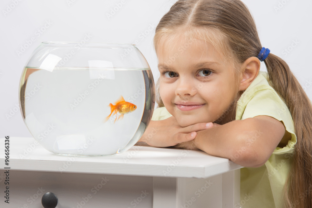 Six year old girl put her head on the handle sitting at the table with an aquarium with goldfish Six year old girl put her head on the handle sitting at the table with an aquarium with goldfish