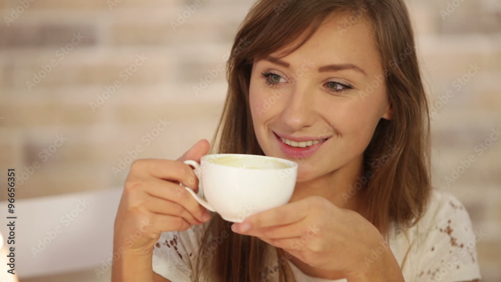 Charming young woman sitting at cafe drinking tea looking at camera and smiling. Panning camera Charming young woman sitting at cafe drinking tea looking at camera and smiling. Panning camera