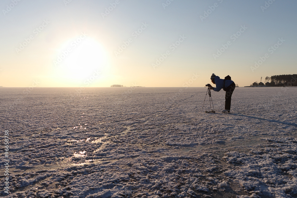 The woman on the skates shooting a sunset on the river river covered with ice and snow