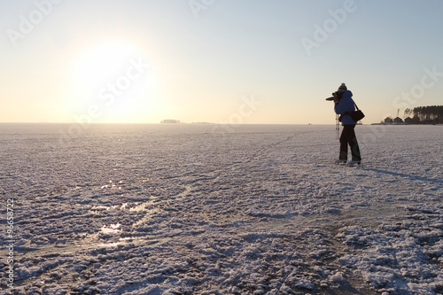 The woman on the skates shooting a sunset on the river river covered with ice and snow © Nataliia Makarova