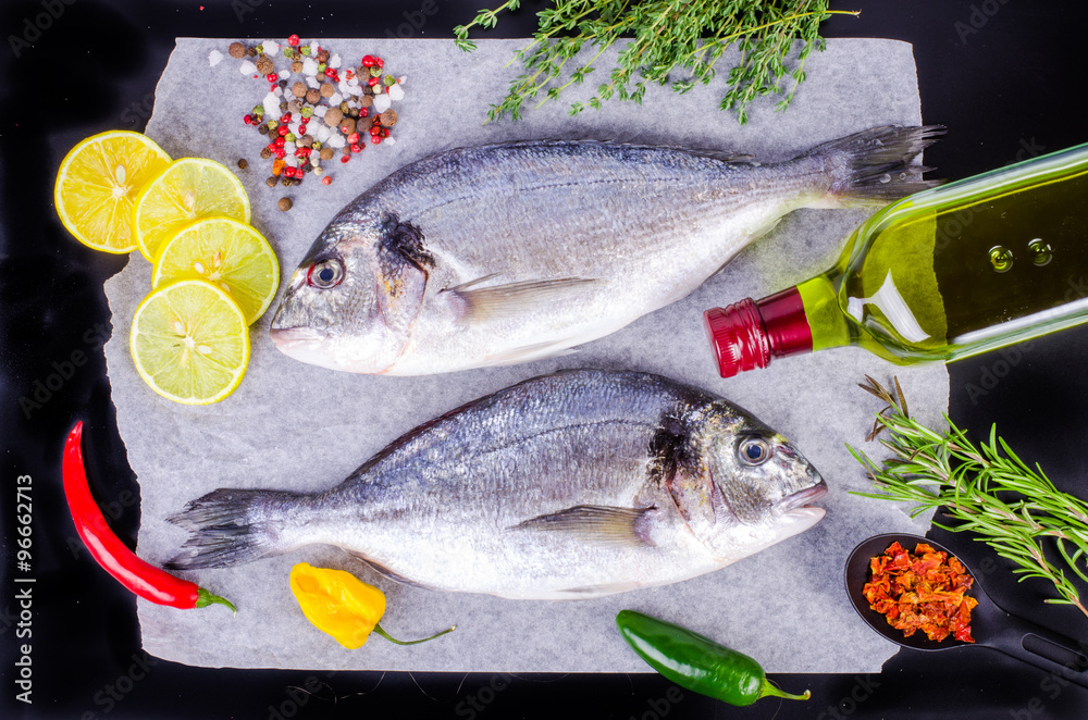 Fresh raw gilthead fishes with lemon, herbs, salt on black background. Healthy food concept. Food frame